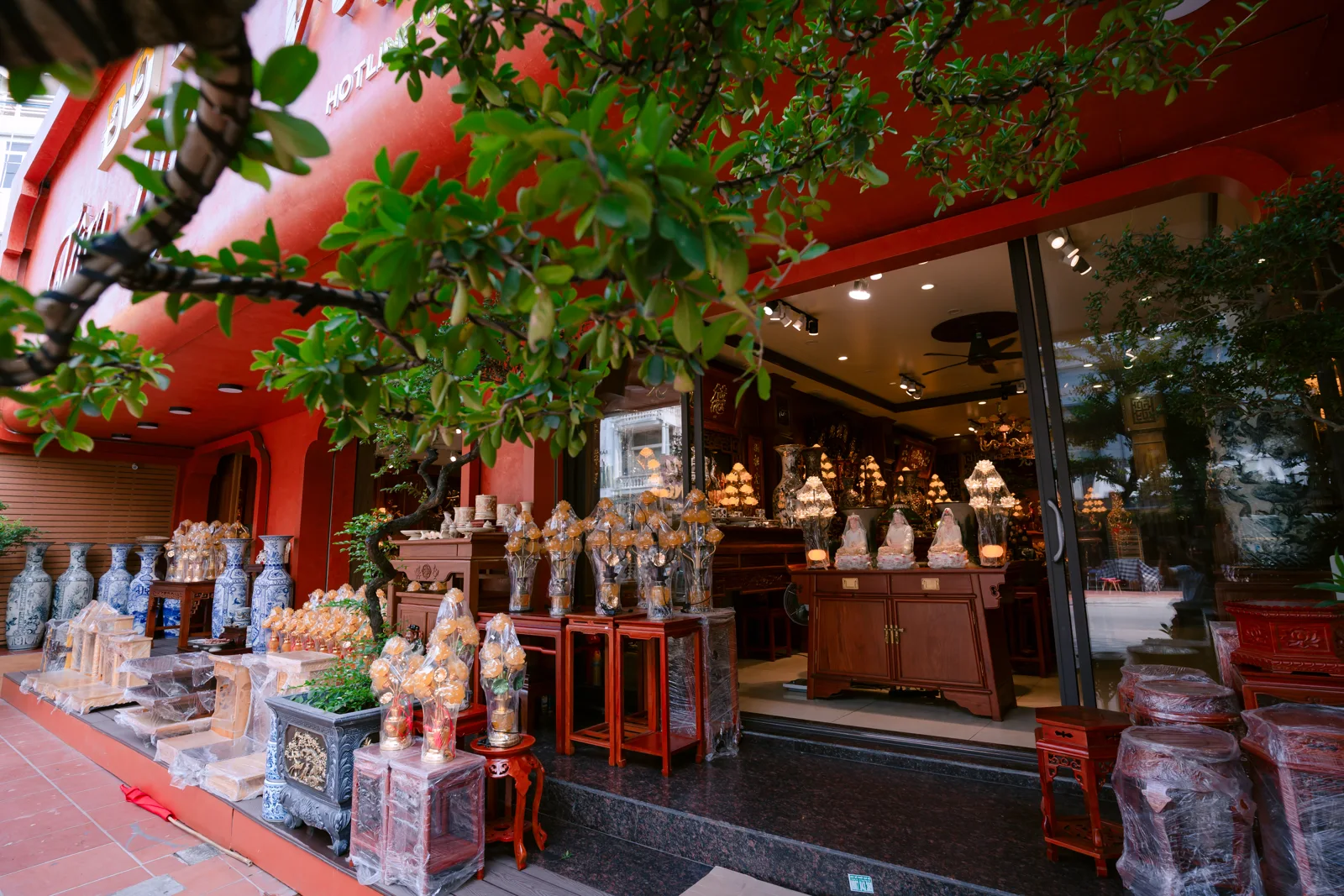 Cửa kính mở của Tâm Linh Việt, bậc tối màu, đồ hình hoa ngoài hiên và tủ cùng đèn sáng bên trong.