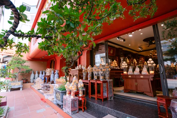 Hiên cửa hàng với hàng bình xanh trắng, cụm hình hoa trên bàn nhỏ, cây trong chậu và gian trưng bày sáng phía sau.