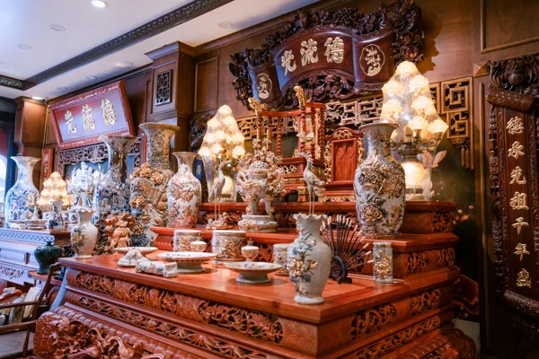 Góc chéo bàn thờ nhiều tầng với mặt bàn chạm dày, bình họa tiết nổi, đỉnh, hạc, đèn và cuốn thư phía trên.