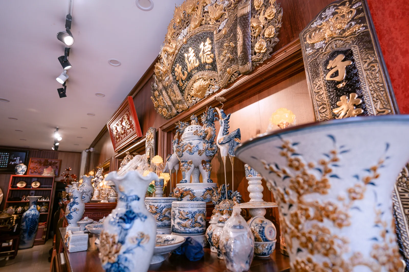 Ảnh cận đồ thờ xanh trắng và vàng, đỉnh có nắp ở giữa, lọ phía trái và một vật miệng loe lớn bị mờ ở tiền cảnh phải.
