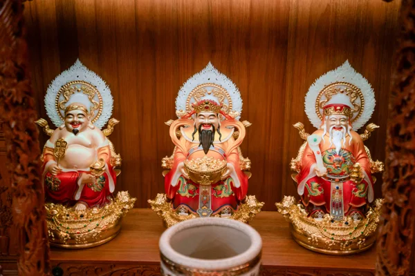Ba tượng áo đỏ nhấn vàng, có nền trang trí trắng phía sau đầu; tượng giữa râu đen cầm vật dạng chậu, hai tượng hai bên khác tư thế.