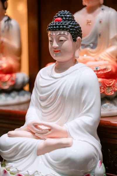 Tượng ngồi áo trắng với hai tay chồng trước bụng, tóc cuộn sẫm điểm đỏ và bệ sen cánh trắng đầu hồng ở mép dưới ảnh.