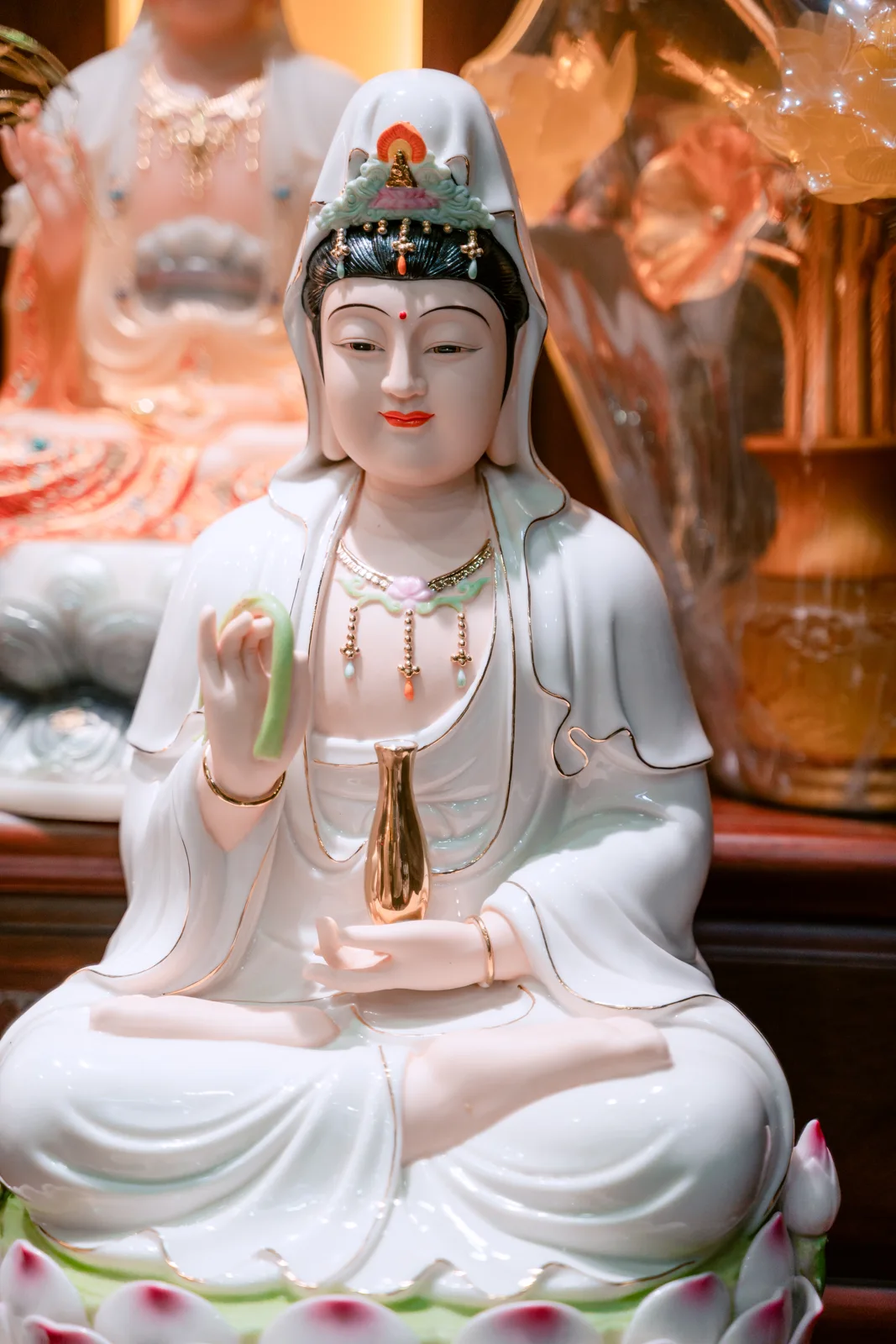Tượng ngồi áo trắng, tay bên trái ảnh giơ lên giữ dải xanh, tay còn lại đỡ bình dáng thon màu vàng; bệ sen trắng điểm hồng.