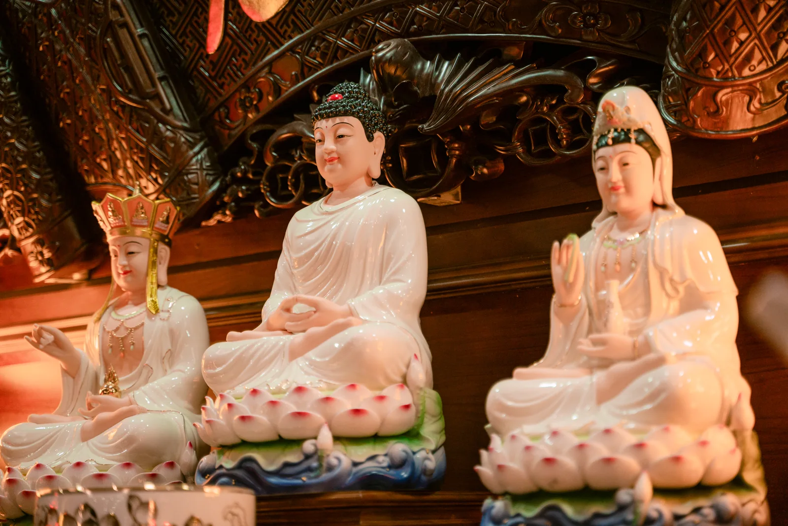 Ba tượng ngồi sáng màu trên bệ sen trắng điểm hồng, nền bệ xanh dạng sóng; tượng giữa tóc cuộn, hai bên có mũ và khăn phủ đầu.