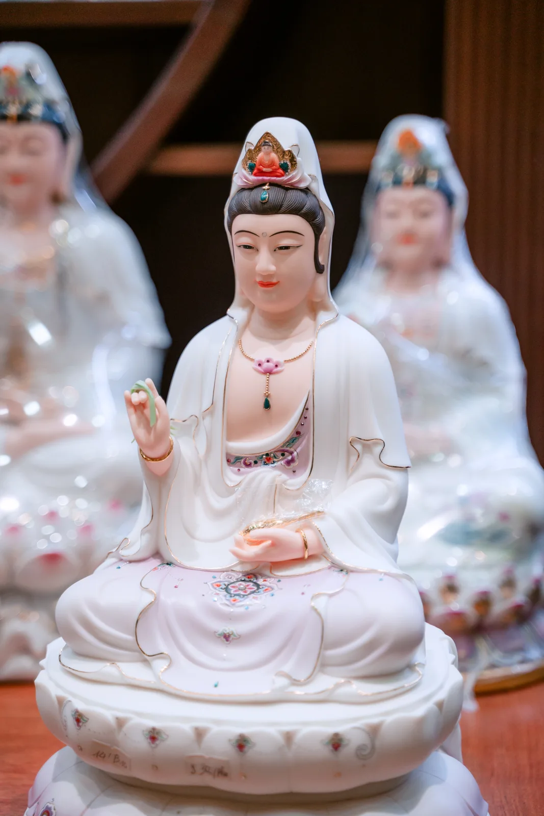 Tượng áo trắng ngồi chính giữa ảnh, môi đỏ, tóc đen dưới khăn trắng, trước cổ có hoa hồng nhỏ và mặt đài có các họa tiết nhỏ.