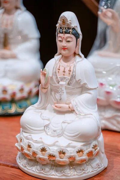 Tượng ngồi áo trắng viền vàng, tay nâng bình trắng có nét hoa sen, đài nhiều lớp cánh điểm vàng cam trên chân đế trắng.