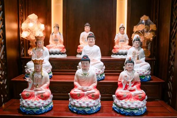 Chín tượng ngồi trưng bày trên ba tầng nền nâu, hàng trước ba tượng áo trắng đỏ, hai bên phía trên có cụm đèn hình hoa.