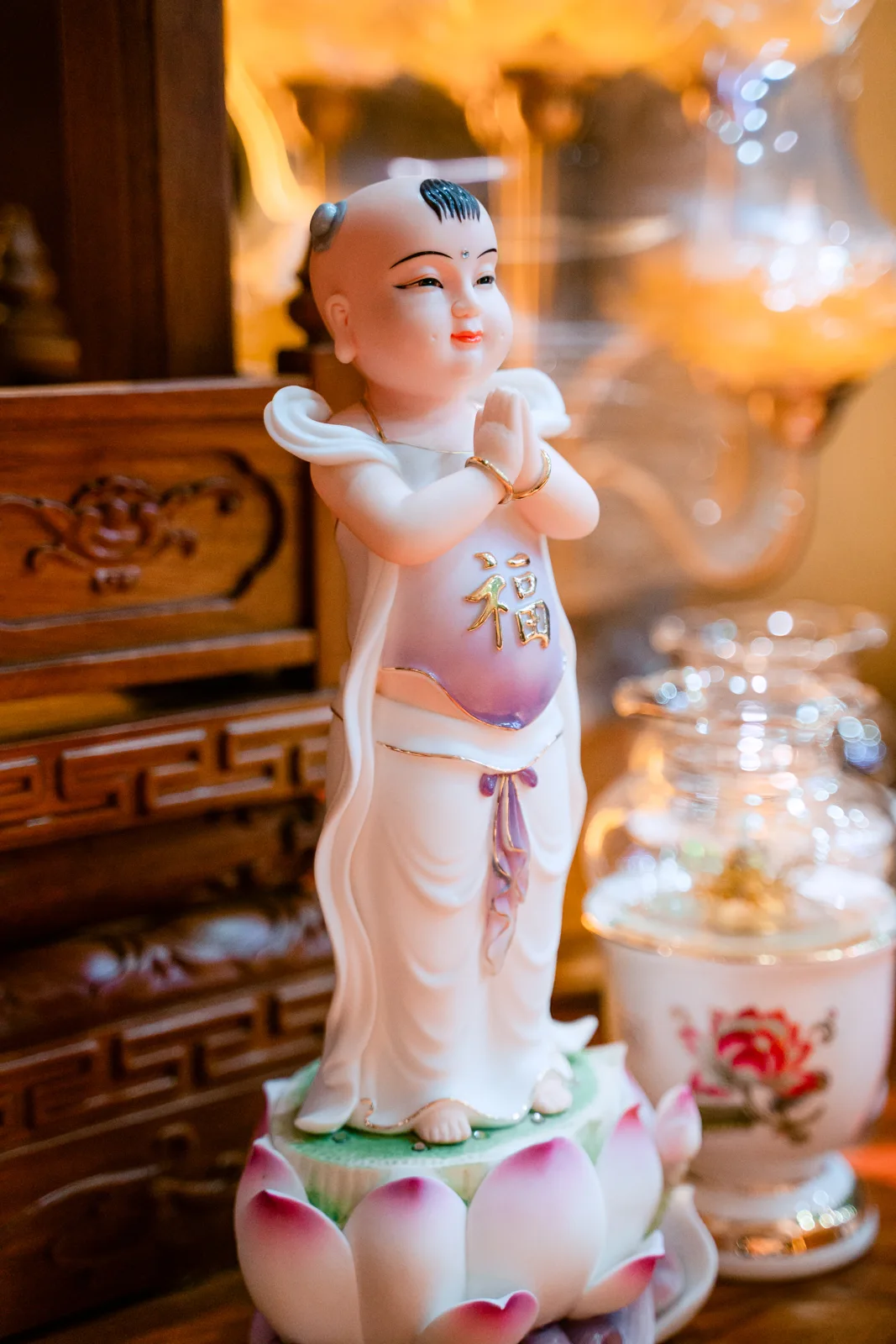 Tượng em bé đầu có chỏm tóc đen, hai tay chắp trước ngực, mặc áo trắng với yếm tím có chữ vàng, đứng trên đài sen hồng trắng.