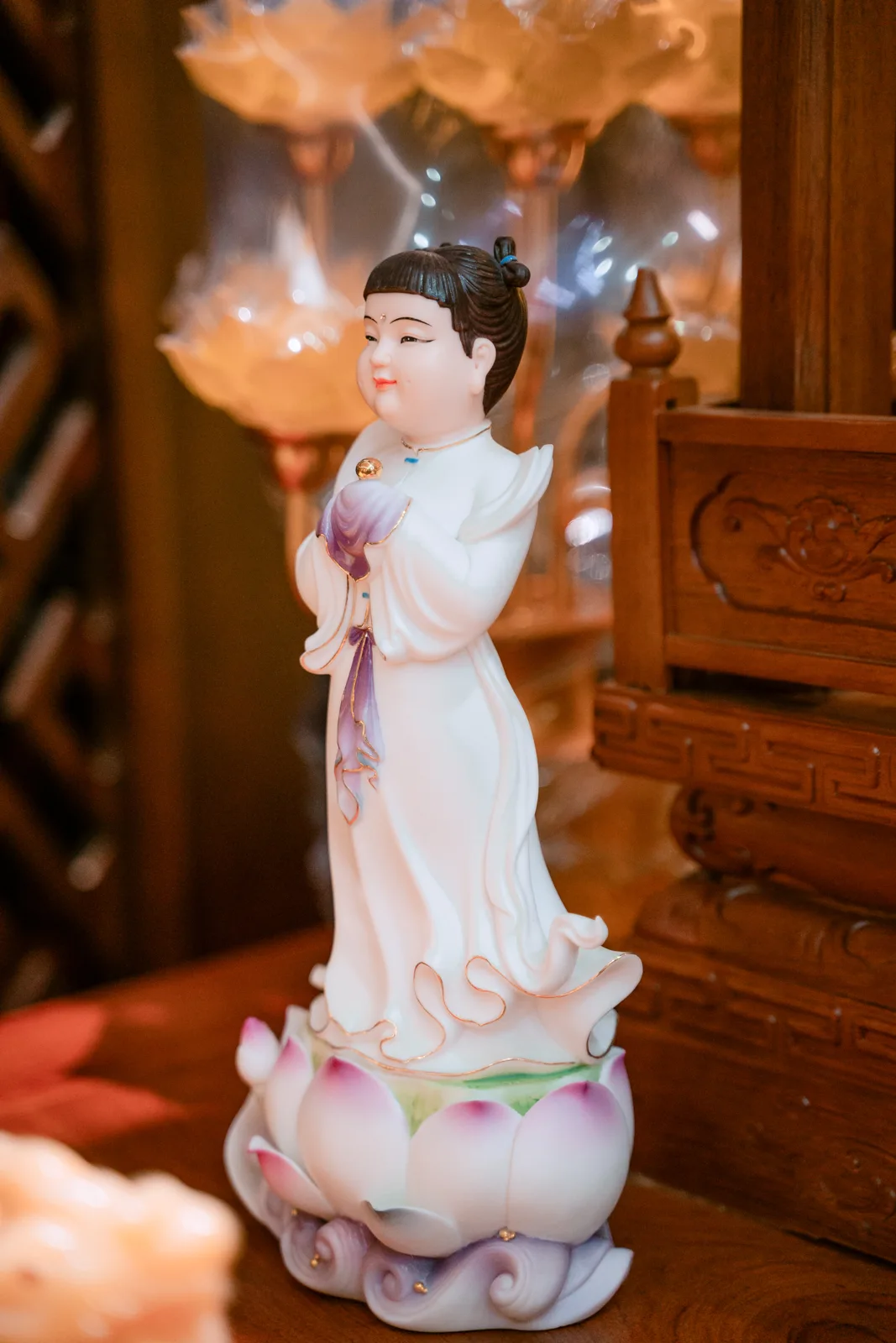 Tượng em bé tóc đen có búi nhỏ, hai tay khép trước ngực trong tay áo tím trắng, áo dài gấu uốn, đứng trên đài sen và chân đế dạng cuộn.