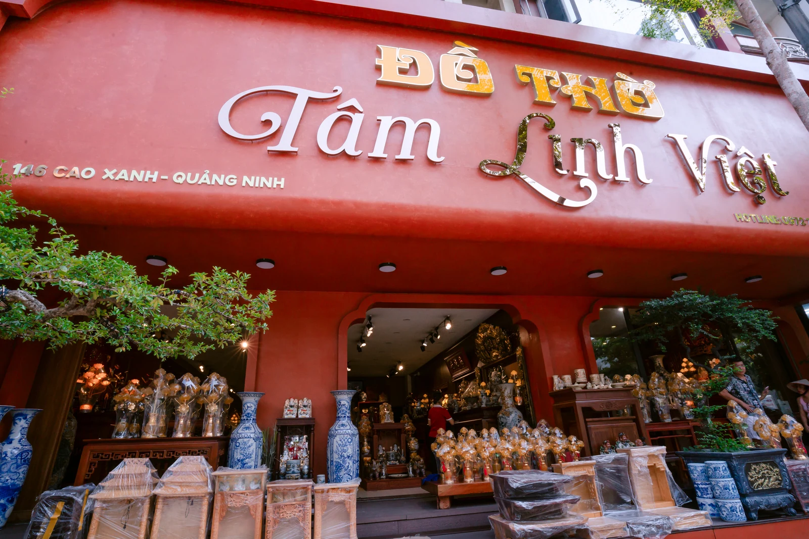 Mặt tiền đỏ Đồ Thờ Tâm Linh Việt với biển chữ lớn, cây xanh, đôi bình xanh trắng và nhiều đồ trưng bày trước cửa.