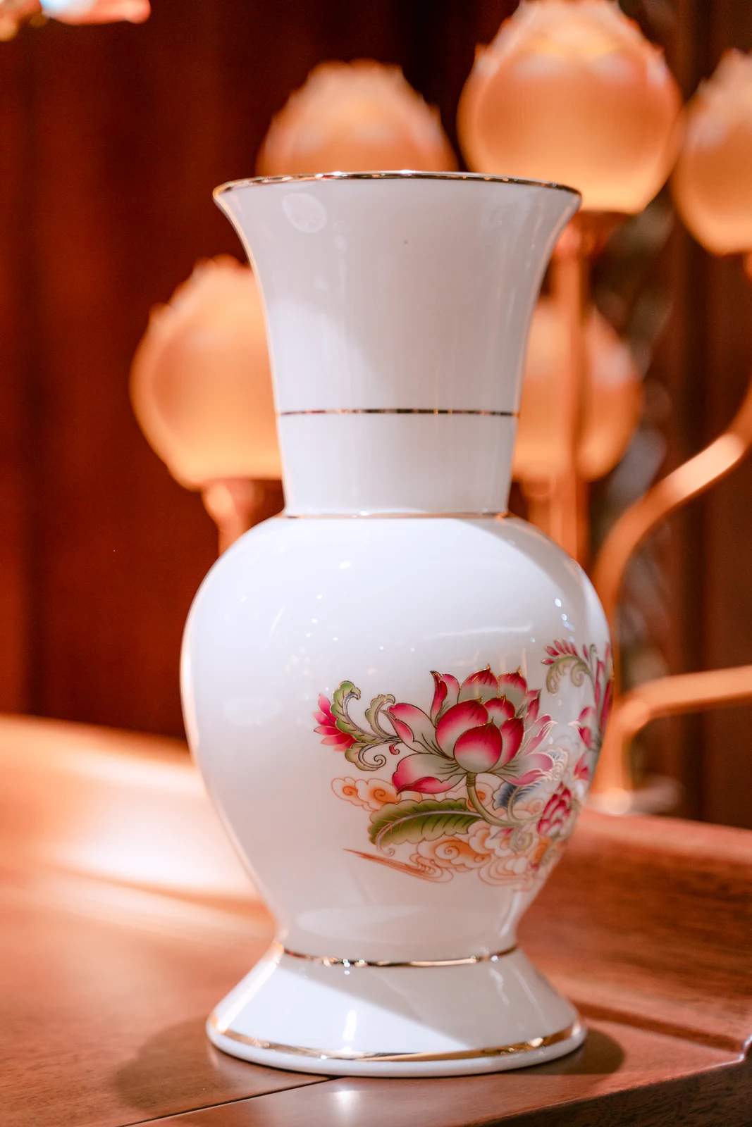 Bình trắng cổ cao miệng loe, thân tròn có hoa sen hồng lá xanh, nhiều đường viền vàng mảnh ở miệng, cổ và chân.
